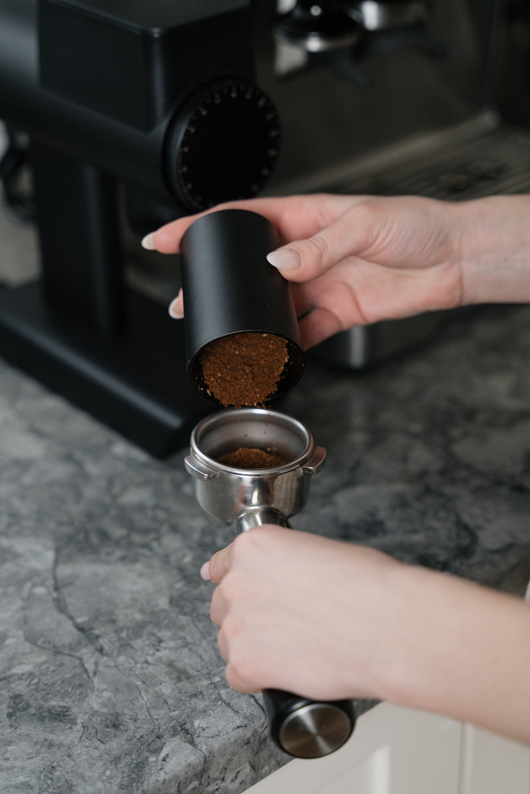 Hands pouring freshly ground coffee into an espresso portafilter